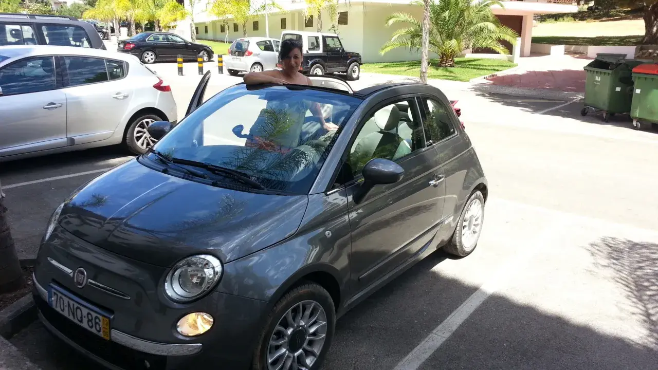 Frau lehnt sich aus einem grauen Fiat 500 Cabrio, bereit für eine Spritztour. Gute mietwagen portugal tipps für den Urlaub!