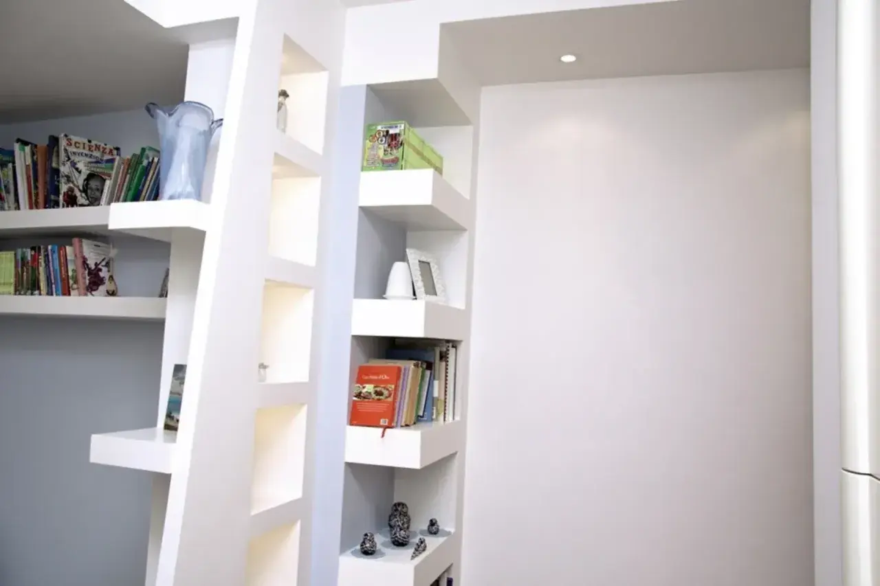 Scaffali moderni in cartongesso, con libri, vasi e soprammobili, creano un angolo lettura accogliente.
