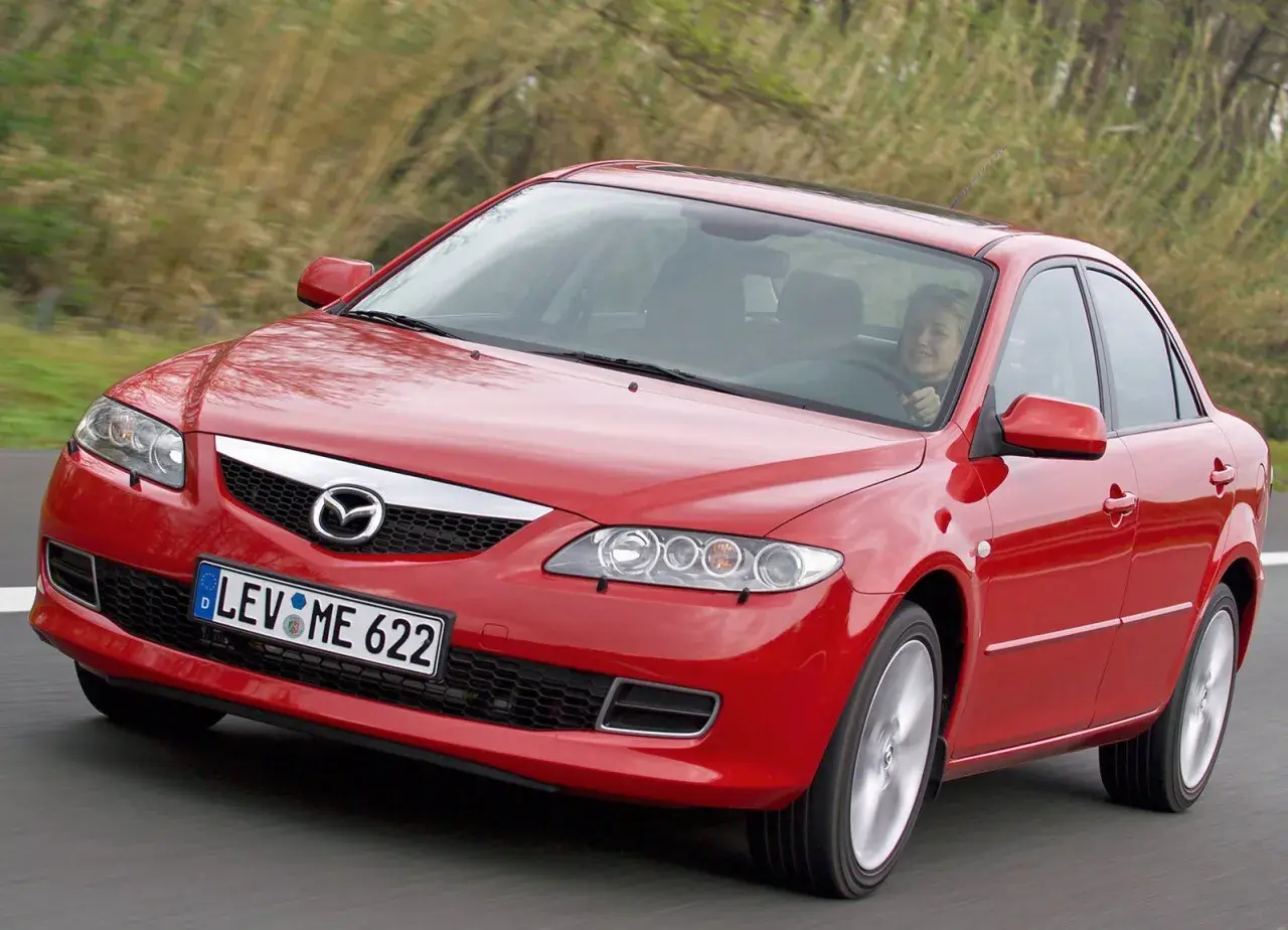 Czerwona Mazda 6 2.0 benzyna w ruchu, za kierownicą uśmiechnięta kobieta.