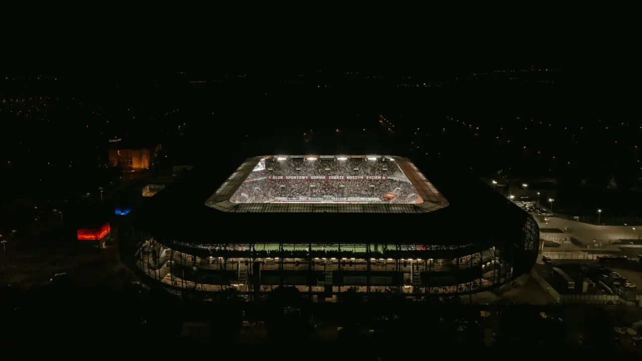 Nocny widok stadionu Górnik Zabrze. Trybuny wypełnione kibicami, widoczny napis "KLUB SPORTOWY GÓRNIK ZABRZE NASZYM ŻYCIEM". Pojemność stadionu robi wrażenie.