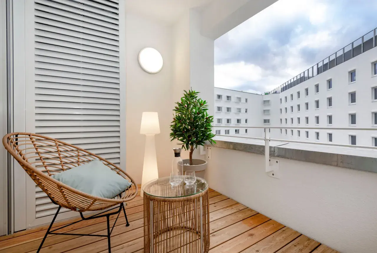 Gemütlicher Balkon mit Holz-Bodenbelag, ideal für eine Mietwohnung. Ein Rattansessel lädt zum Entspannen ein.