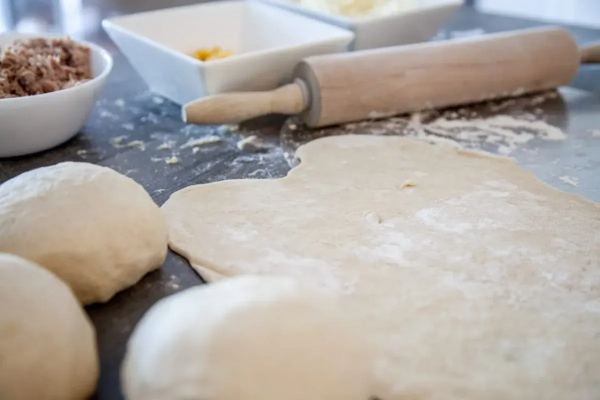 Pizzateig, Nudelhölzer und Schüsseln mit Zutaten auf einer Arbeitsfläche.