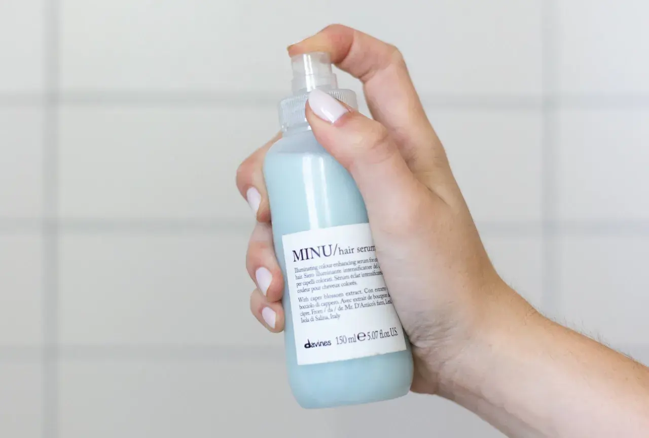 Mano che spruzza siero per capelli MINU. Scopri come si usa il siero per capelli per un colore luminoso e intenso.