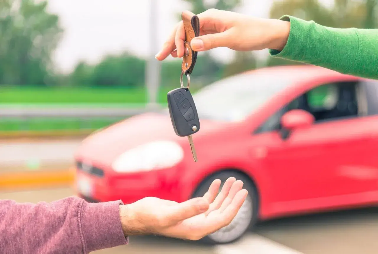 Passaggio di chiavi auto, un gesto che simboleggia cosa serve per vendere auto: fiducia e un nuovo inizio su quattro ruote rosse.