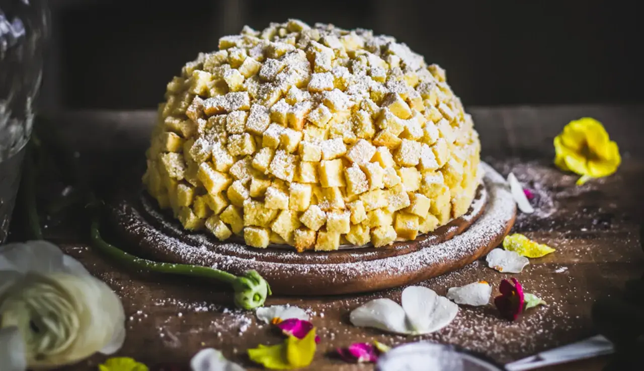 Torta mimosa, una delizia soffice ricoperta di cubetti di pan di Spagna e zucchero a velo, pronta per essere gustata.