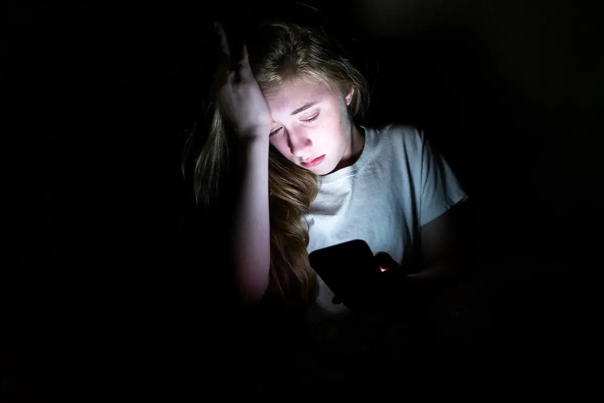 En tonåring med handen mot pannan, upplyst av en mobilskärm. Känslan av depression hos barn kan testas genom att observera sådana här stunder.