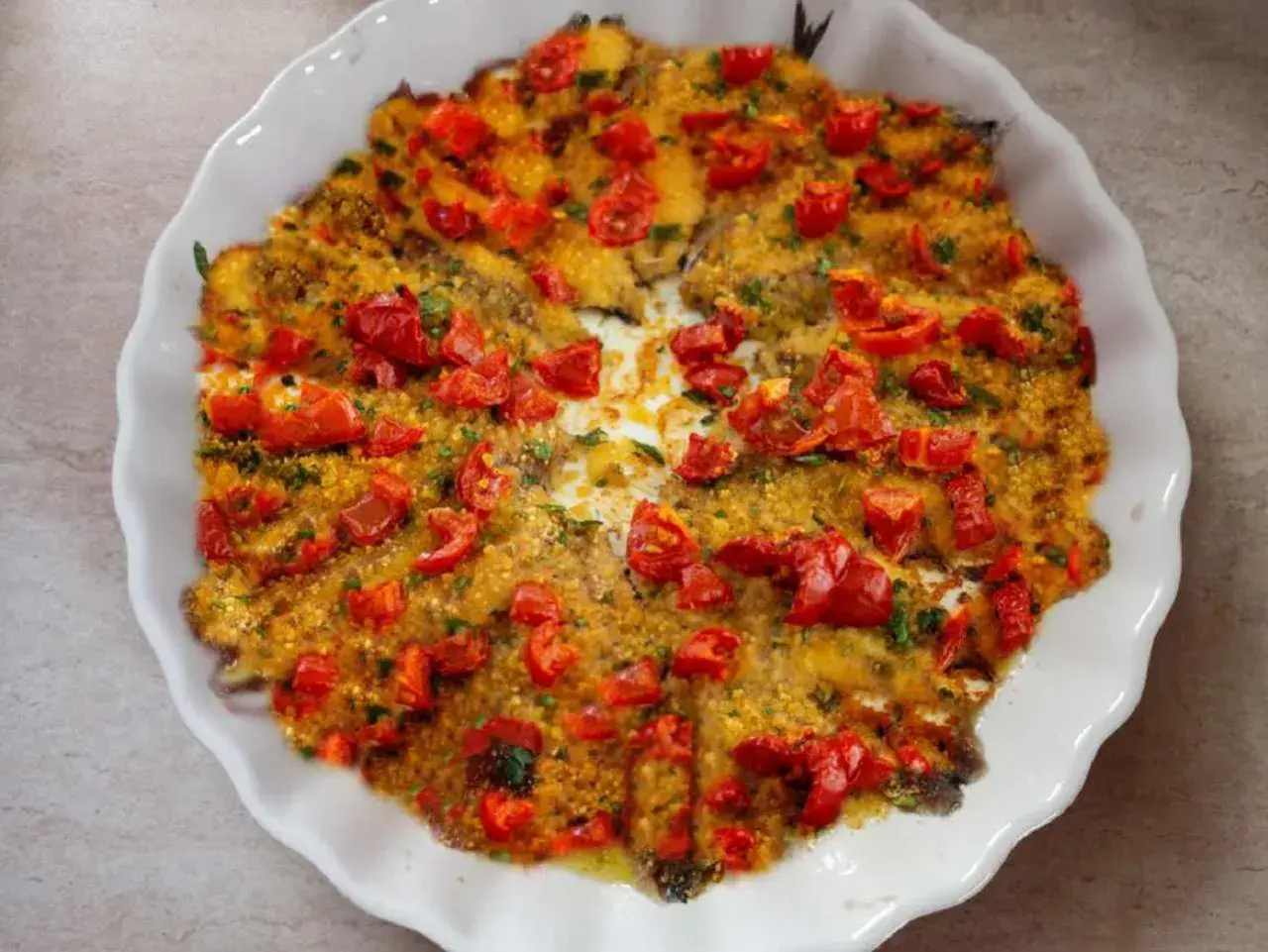 Alici al forno dorate e succulente, ricoperte di pomodorini freschi e pangrattato croccante. Un piatto semplice e gustoso.