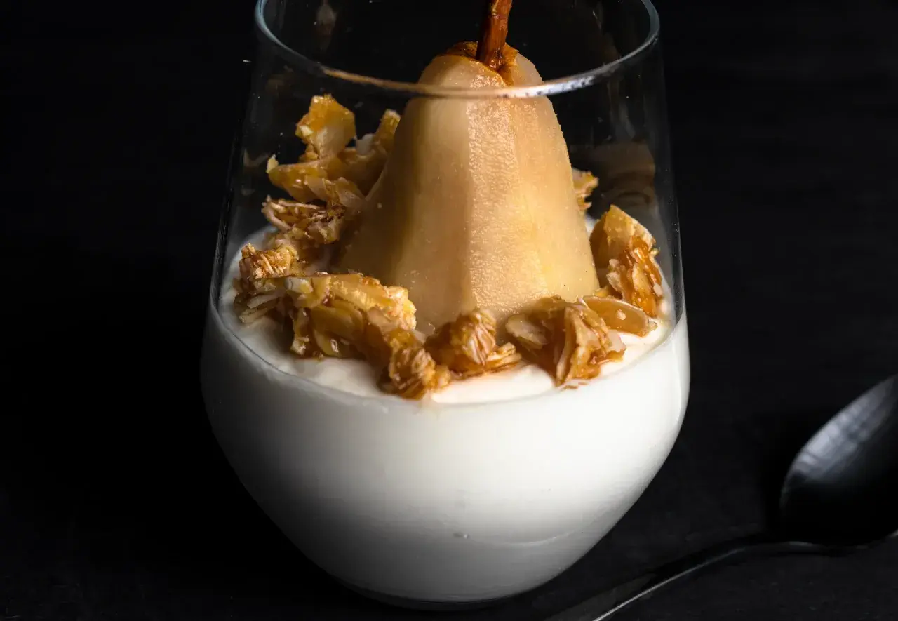 Ein köstlicher Nachtisch mit einer ganzen Birne auf cremigem Joghurt, garniert mit karamellisierten Nüssen.