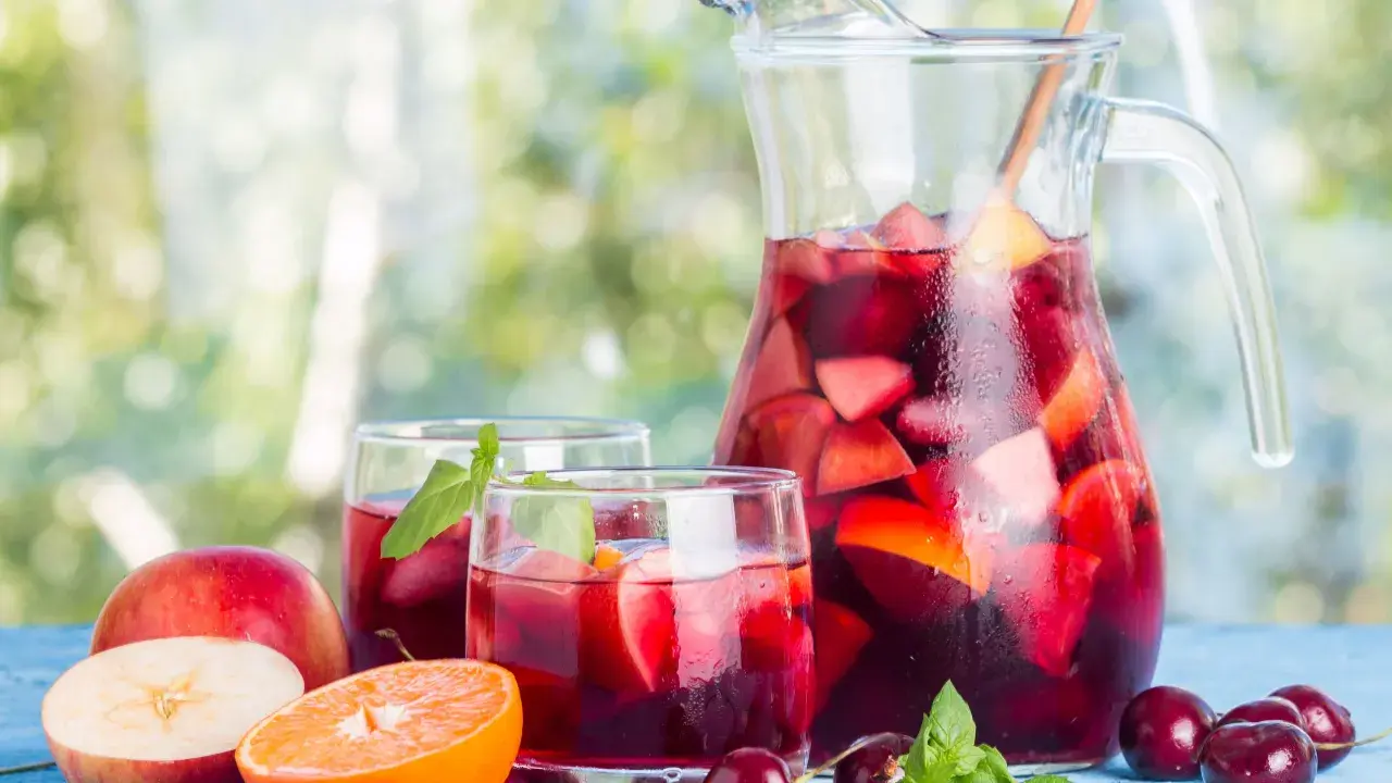 Caraffa e bicchieri pieni di sangria, con frutta fresca come mele, arance e ciliegie. Perfetta per fare la sangria in una giornata estiva.