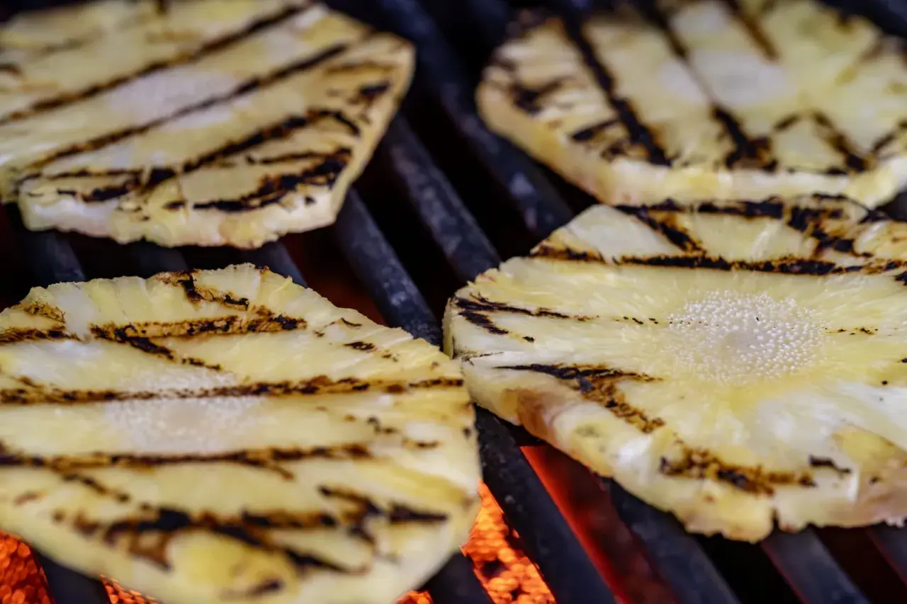 Tranches d'ananas barbecue grillées, avec des marques de cuisson foncées sur fond de braises rougeoyantes.