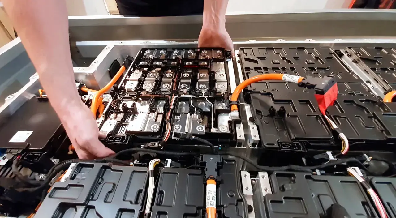 Manos trabajando en el interior de un paquete de baterías de coche eléctrico. Averiguar cuanto cuesta cambiar la bateria del coche es clave.
