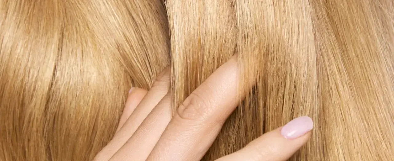 Dita accarezzano capelli biondi e setosi. Posso usare la maschera per capelli prima dello shampoo per ottenere questa morbidezza.