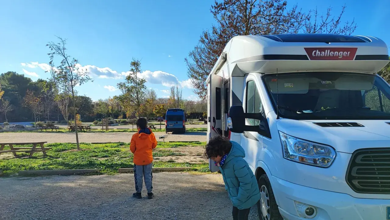 Deux enfants devant un camping-car Challenger, en route pour une aventure dans le sud de la France. Le soleil brille, les arbres perdent leurs feuilles.