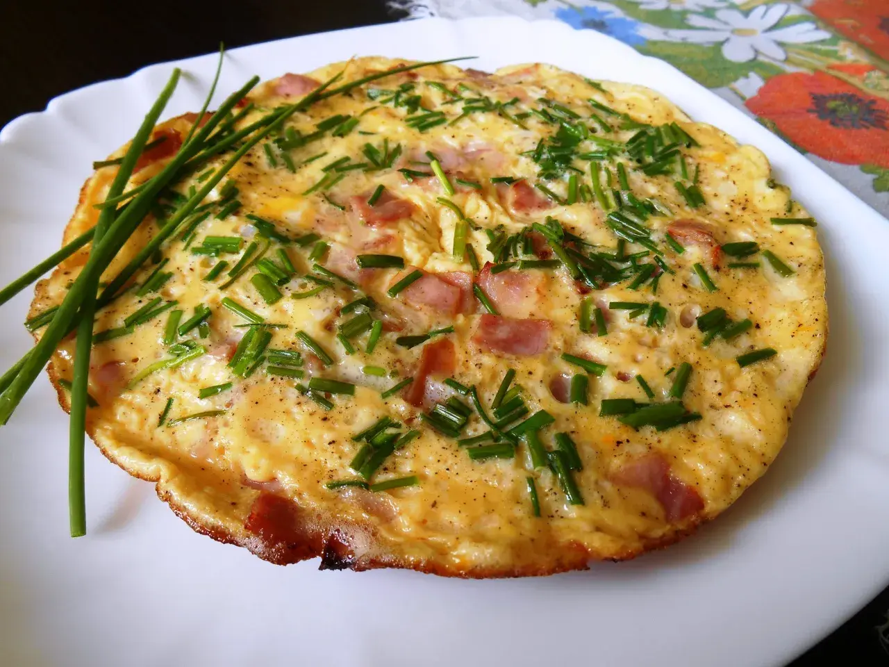 Puszysty omlet ze szczypiorkiem i kawałkami wędliny, podany na białym talerzu.