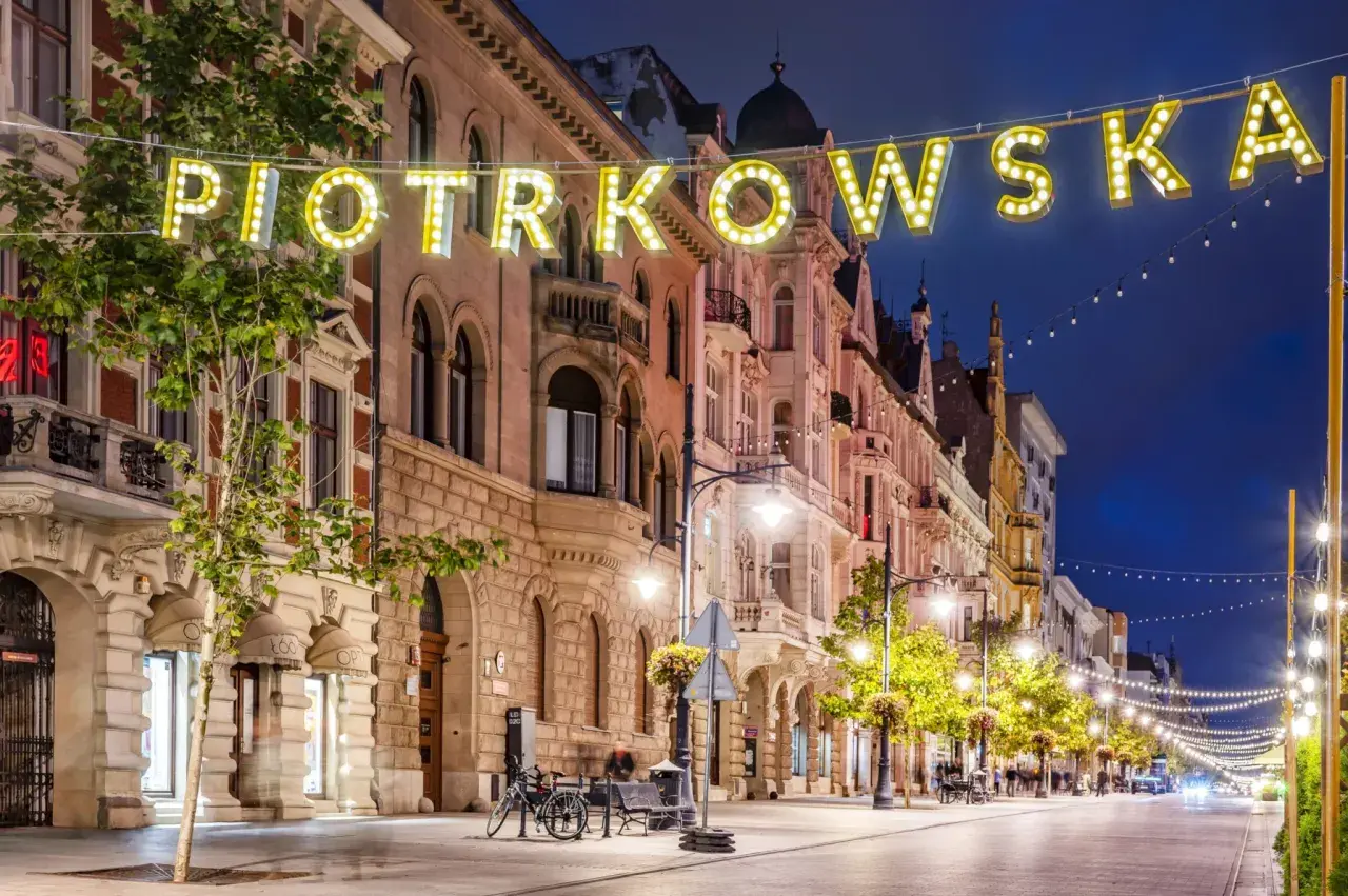 Ulica Piotrkowska nocą, iluminowana neonami i girlandami świateł. Idealne miejsce, by poczuć klimat Łodzi i zastanowić się, co zwiedzić w Łodzi.