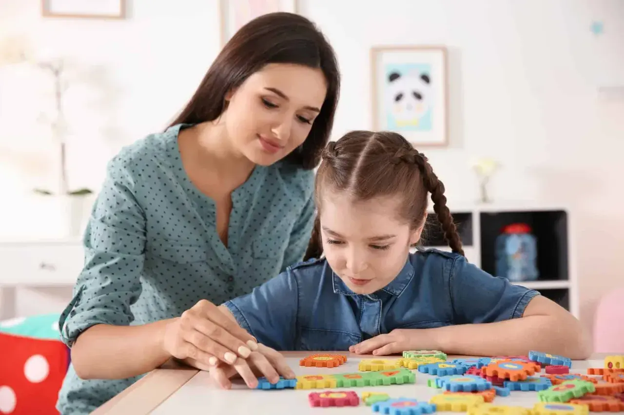 Terapeutka pomaga dziewczynce z upośledzeniem w stopniu umiarkowanym układać kolorowe puzzle.