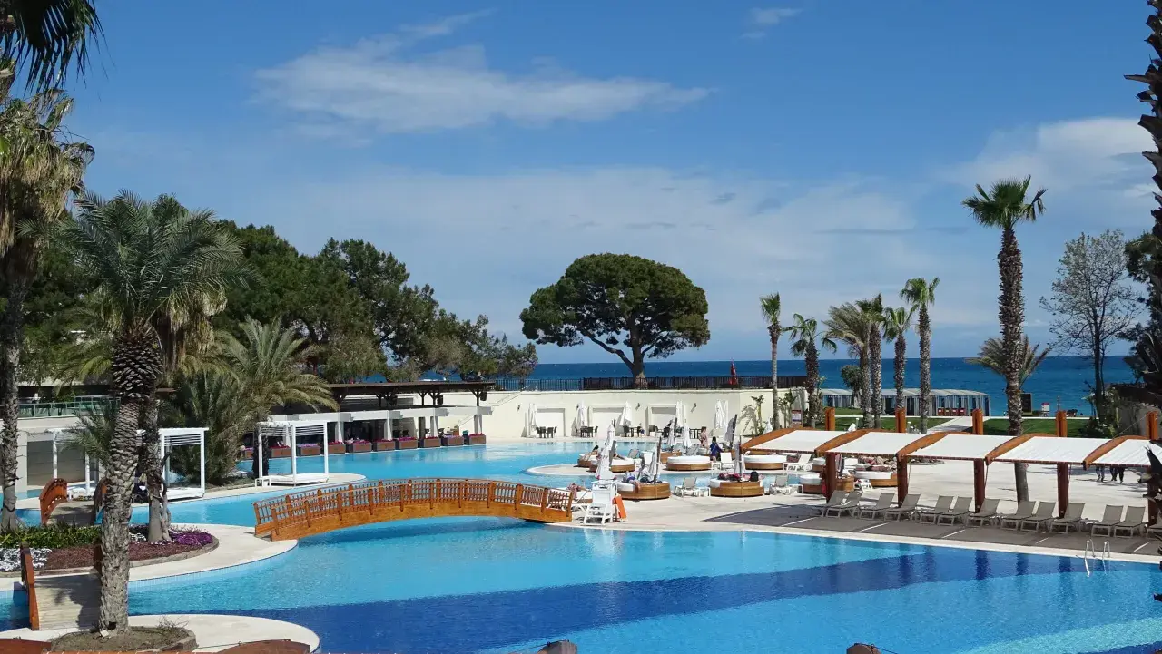 Luksusowy basen z drewnianym mostkiem i palmami, idealne miejsce na relaks w Rixos Turcja.