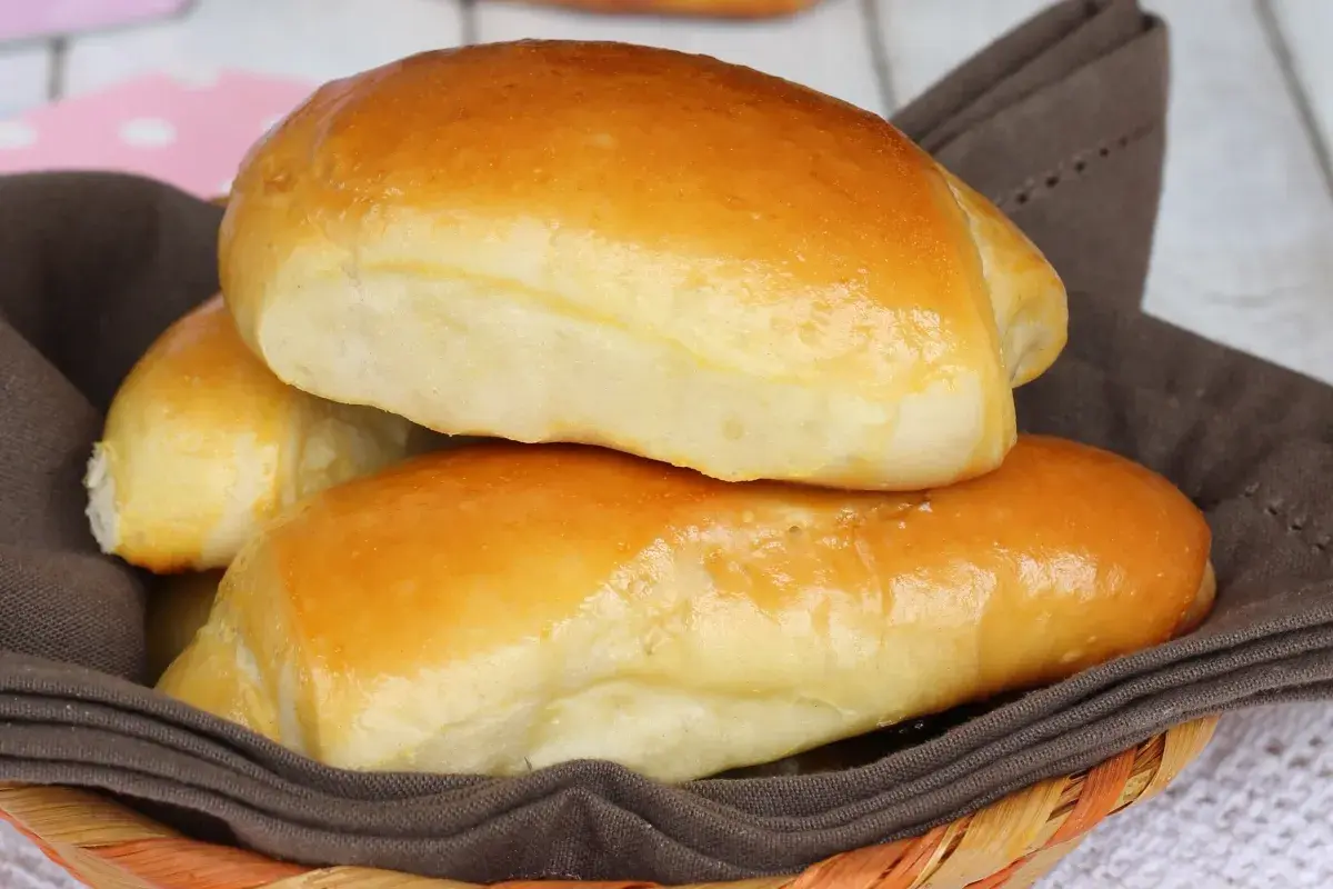 Deliziosi panini al latte dorati, morbidi e invitanti, serviti in un cestino foderato con un tovagliolo marrone.