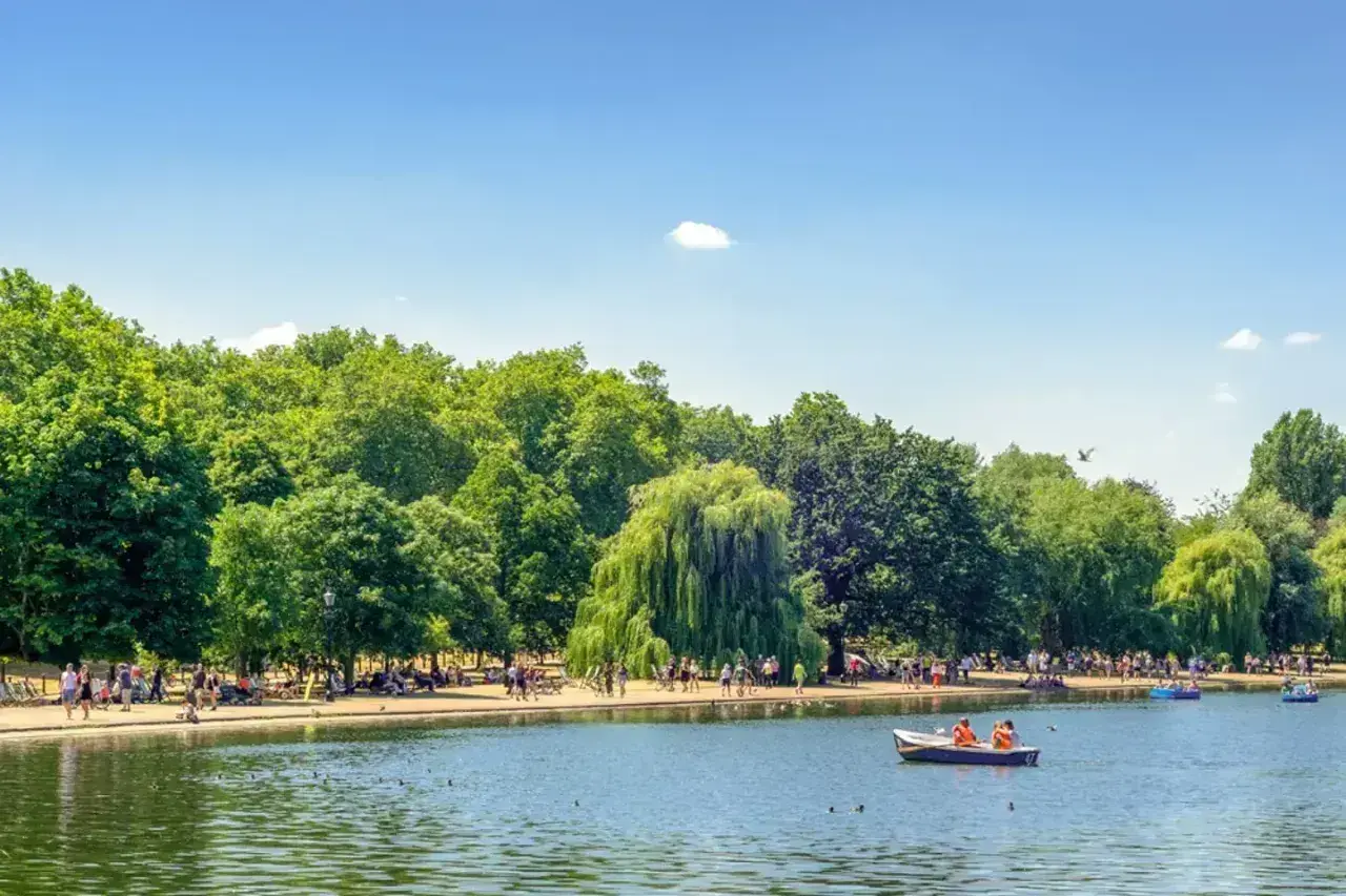 Słoneczny dzień w Hyde Park w Londynie. Ludzie odpoczywają nad jeziorem, niektórzy pływają łódkami.