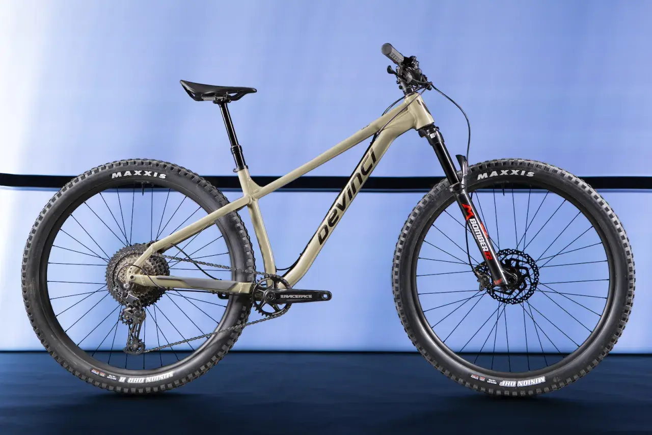 A tan Devinci Kobain mountain bike with Maxxis tires and a Marzocchi Bomber fork, ready for any trail.