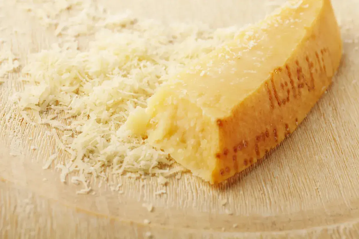 Ein Stück Parmesan mit geriebenem Käse daneben. Die Rinde ist deutlich geprägt und zeigt, dass die **Parmesanrinde essbar** ist.