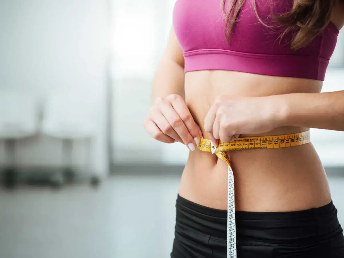 Une femme mesure sa taille avec un mètre ruban. La question "peut on maigrir sans sport" est au cœur de cette image de perte de poids.