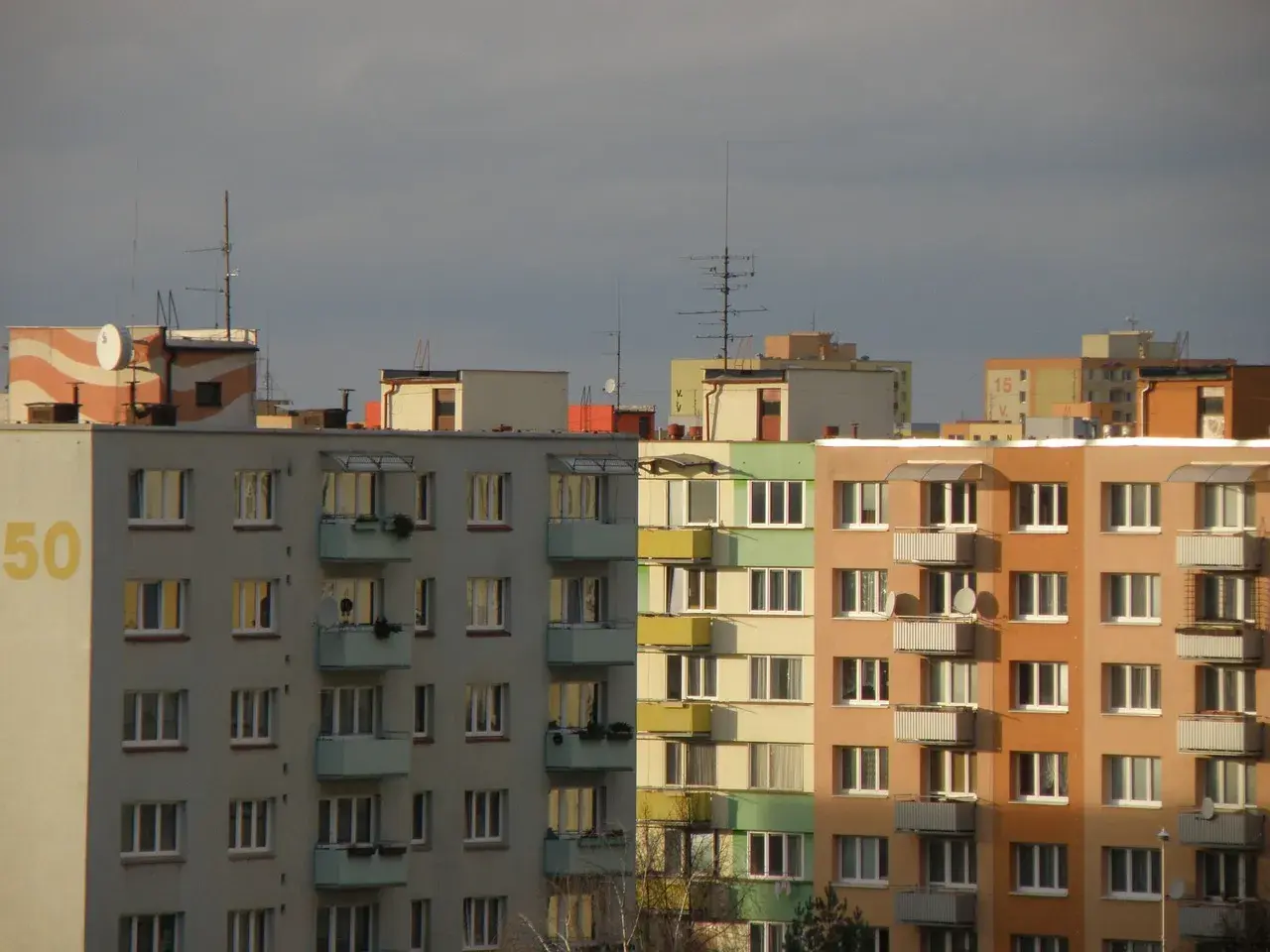 Bloki mieszkalne z balkonami, na dachu jeden z nich widnieje napis "50". W tle inne budynki, niebo zachmurzone. Warto pamiętać o fundusz remontowy przepisy.