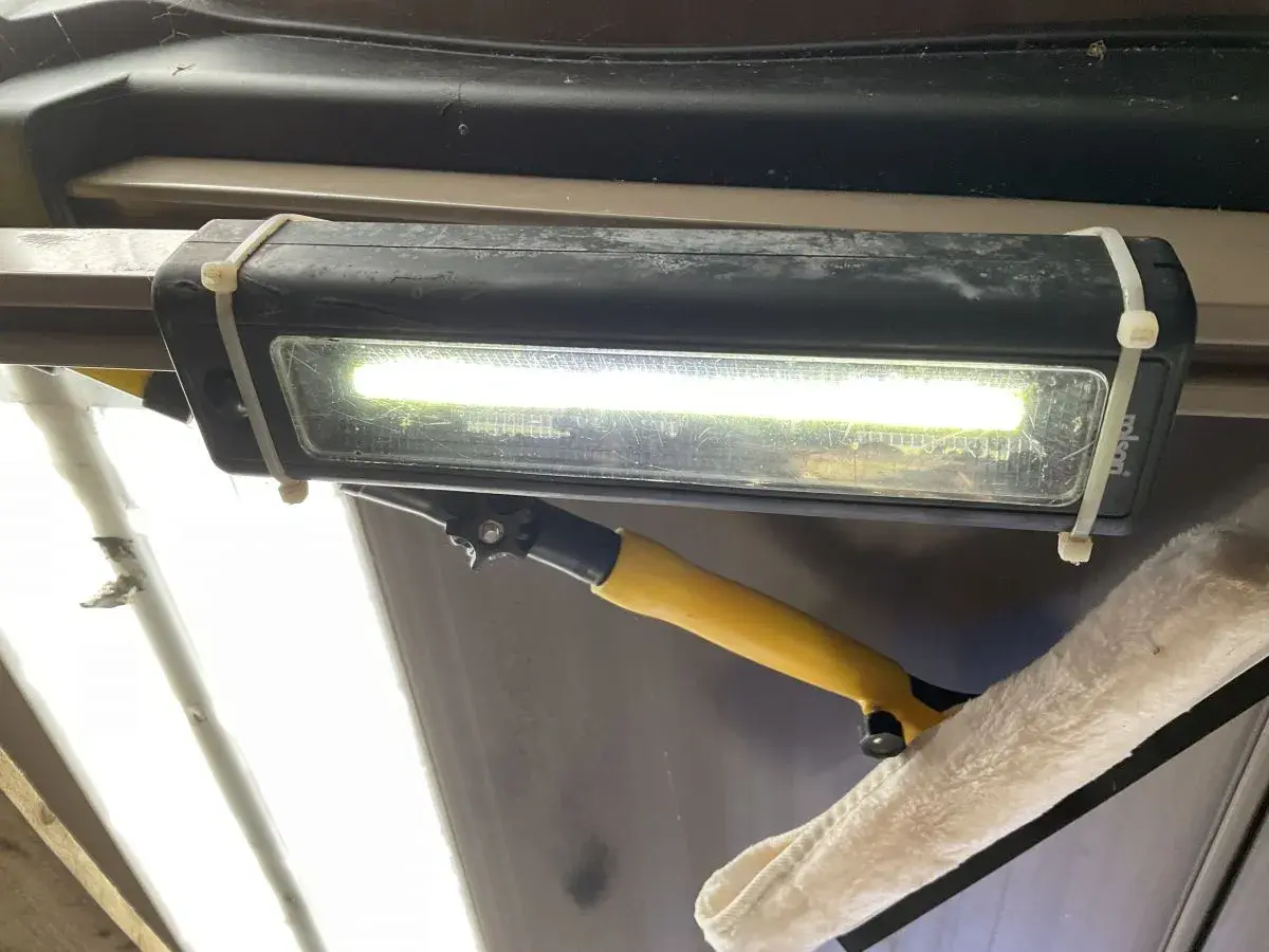 Jasne, oto opis:

Oświetlenie garażu bez prądu: prowizoryczna lampa LED na opaskach zaciskowych, oświetlająca wnętrze. Obok wisi narzędzie do czyszczenia.