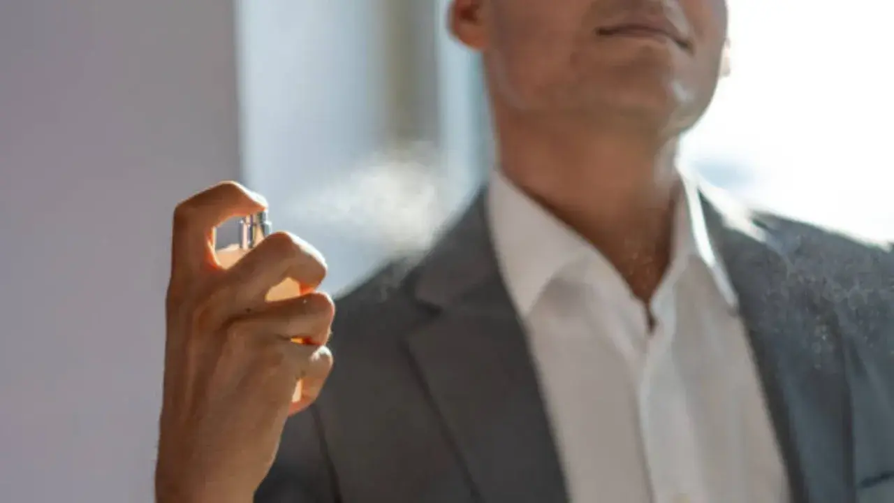 Hombre aplicándose perfume con un frasco rociador.