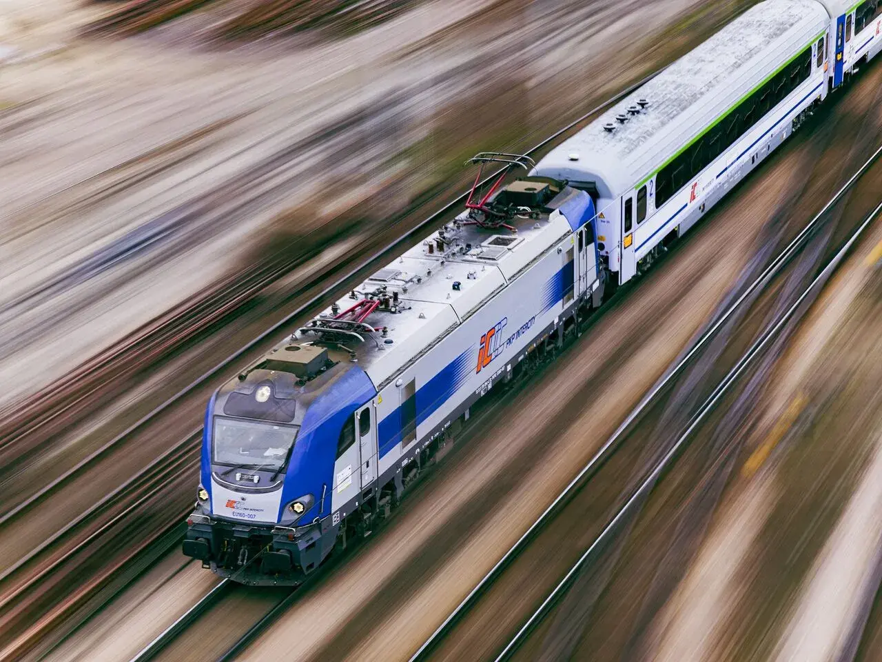 Pędzący pociąg PKP Intercity EU160 na torach, rozmyte tło sugeruje dużą prędkość.