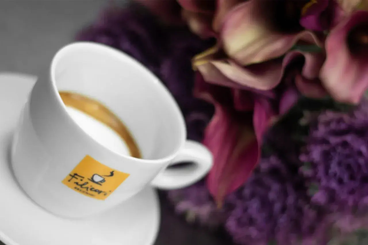 Tazza di caffè con logo Filicori. Un macchiatone o un macchiato? La bellezza dei fiori viola fa da sfondo.