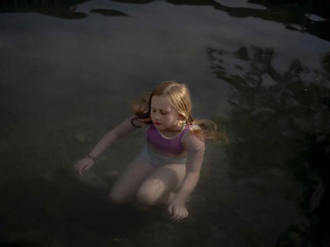 Bambina con capelli biondi immersa nell'acqua scura, un'immagine che evoca la serenità e la purezza, tipica delle opere di Laura Pannack.