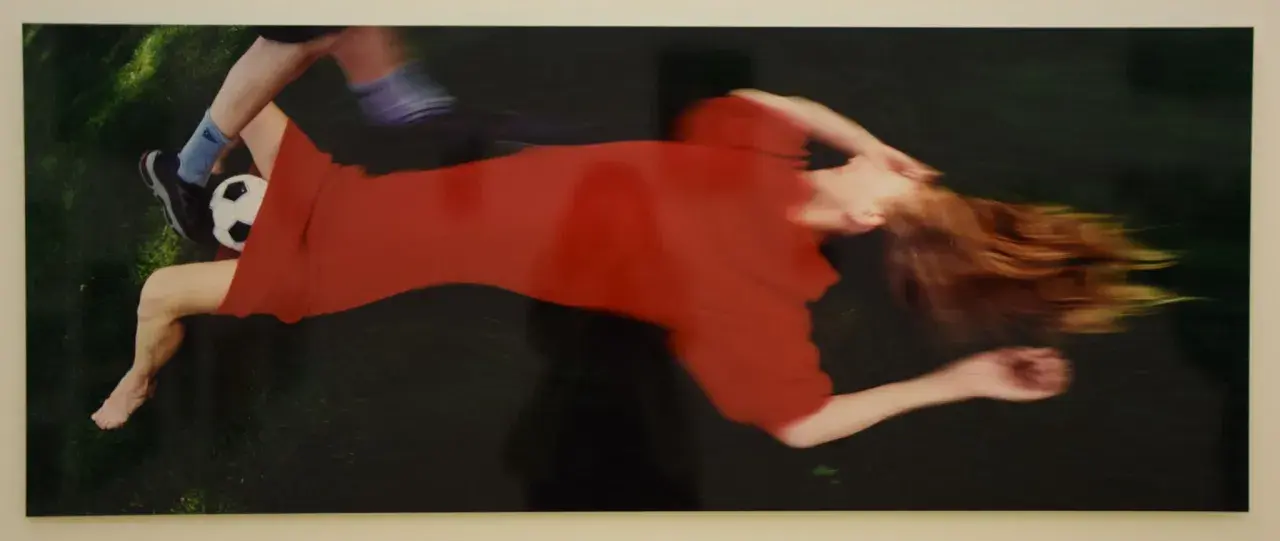 Boris Mikhailov cattura un momento di movimento sfocato: una donna in abito rosso e un piede con pallone da calcio.