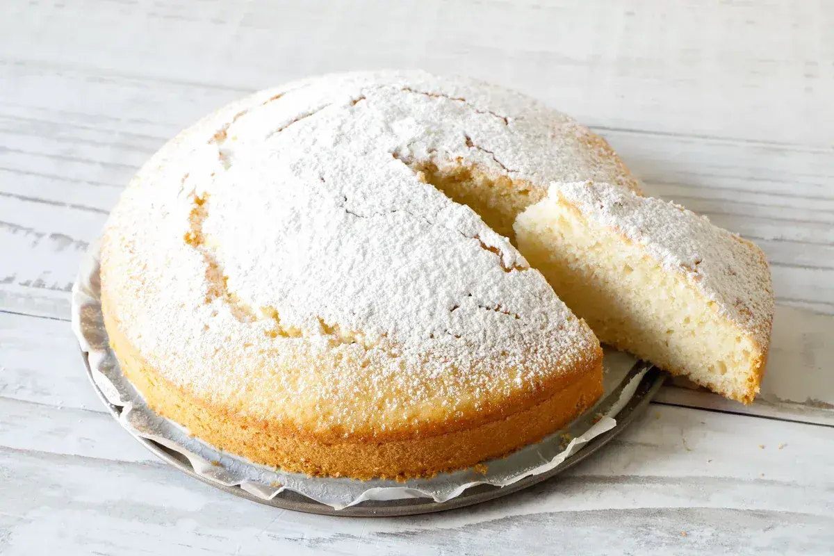 Una soffice torta all'acqua, cosparsa di zucchero a velo, con una fetta tagliata che ne mostra la morbidezza.