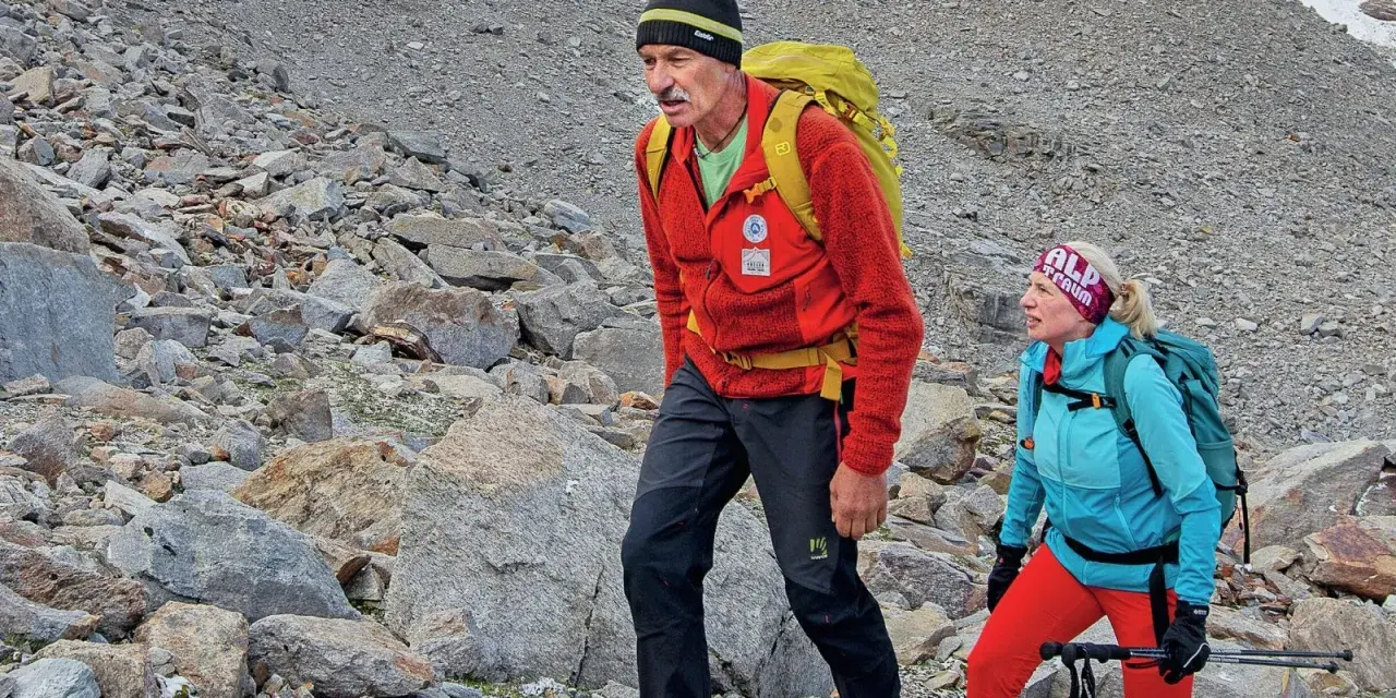 Simon Gietl und eine Frau wandern auf einem felsigen Berghang. Sie tragen Rucksäcke und Wanderkleidung.