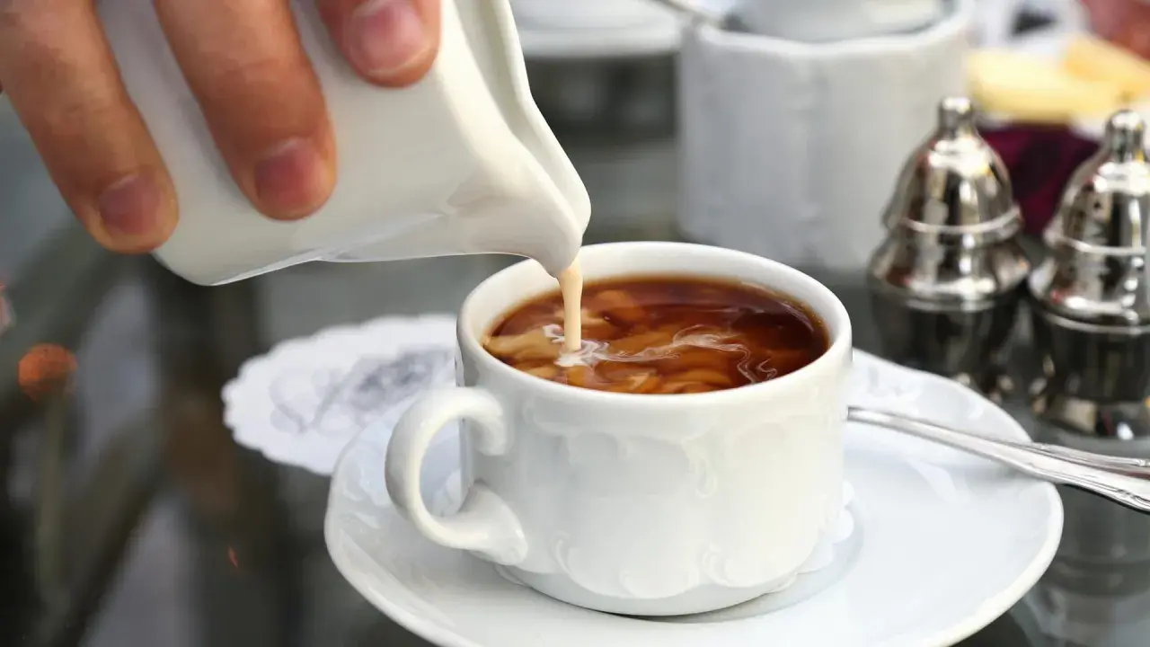 Ein Schwall Milch fließt in eine Tasse filterkaffee mit milchschaum. Ein Moment der Ruhe vor dem ersten Schluck.