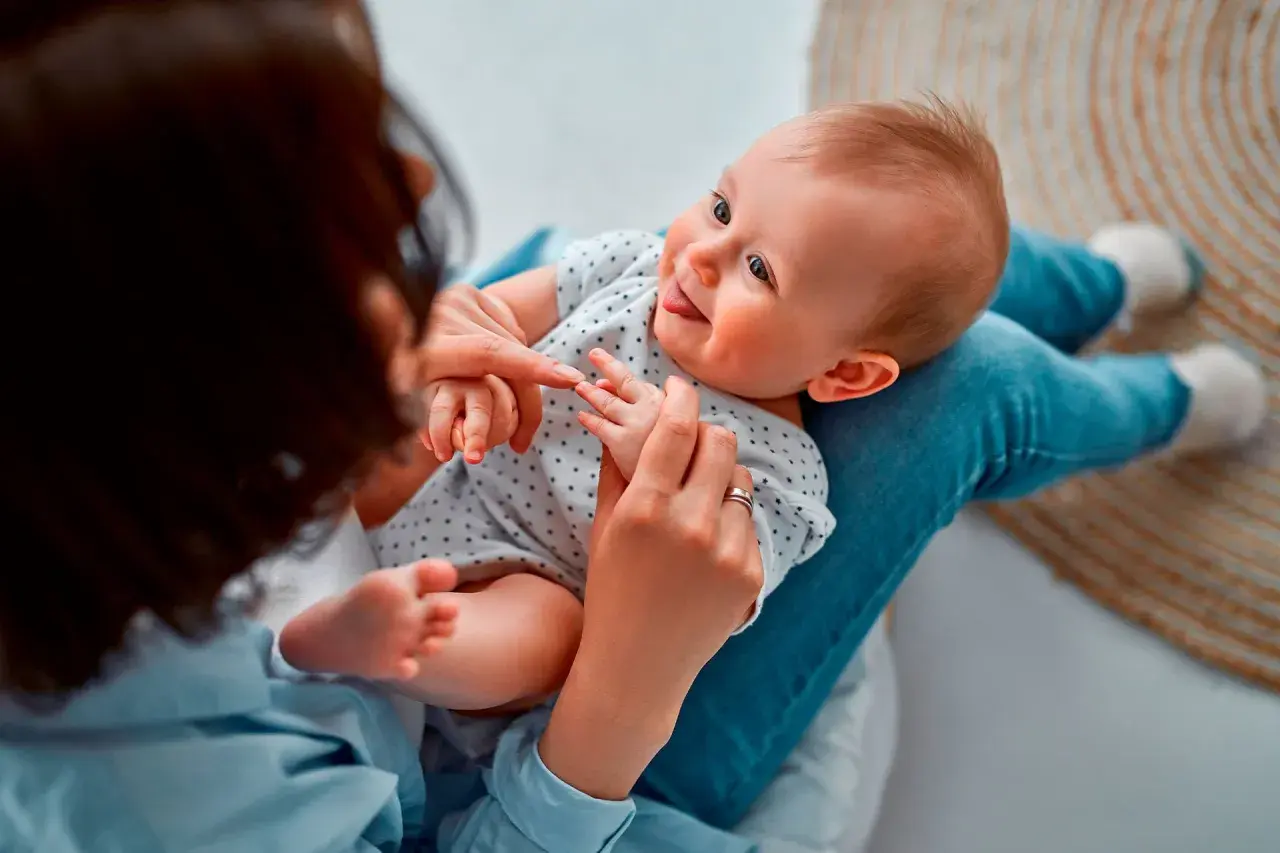 Madre juega con su bebé, enseñándole sus deditos. El bebé sonríe, quizás practicando sus primeras palabras.