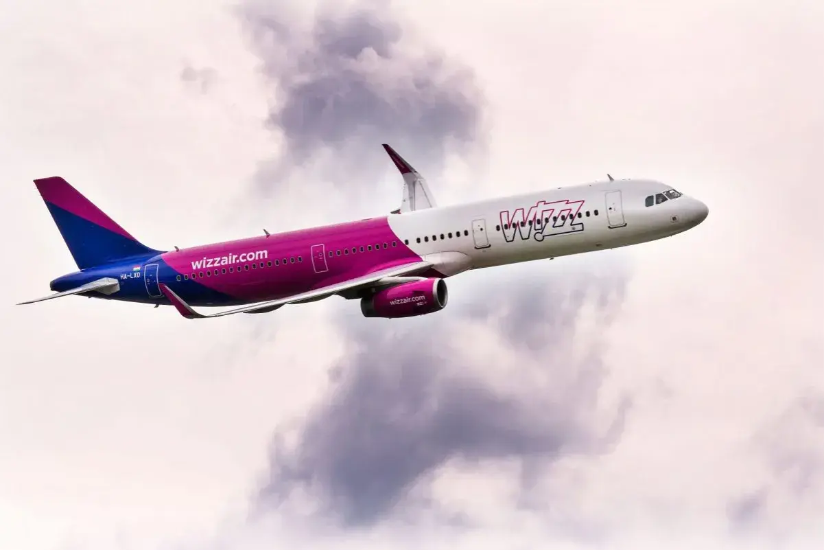 Samolot Wizz Air z charakterystycznym różowym pasem wznosi się na tle chmur. Wizz flex to jego motto!