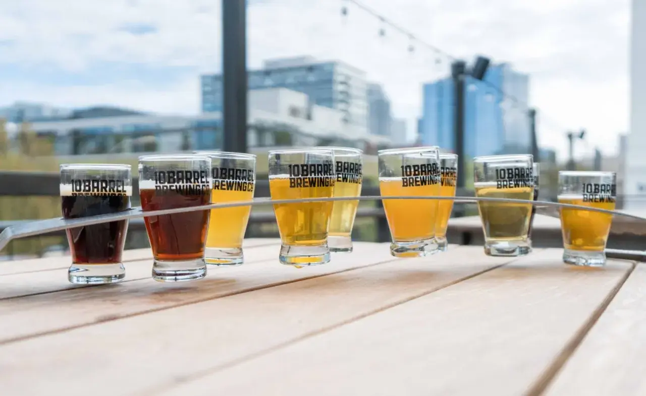 Un assortiment de bières, dont une délicieuse sour ale, sur une table en bois avec des bâtiments en arrière-plan.
