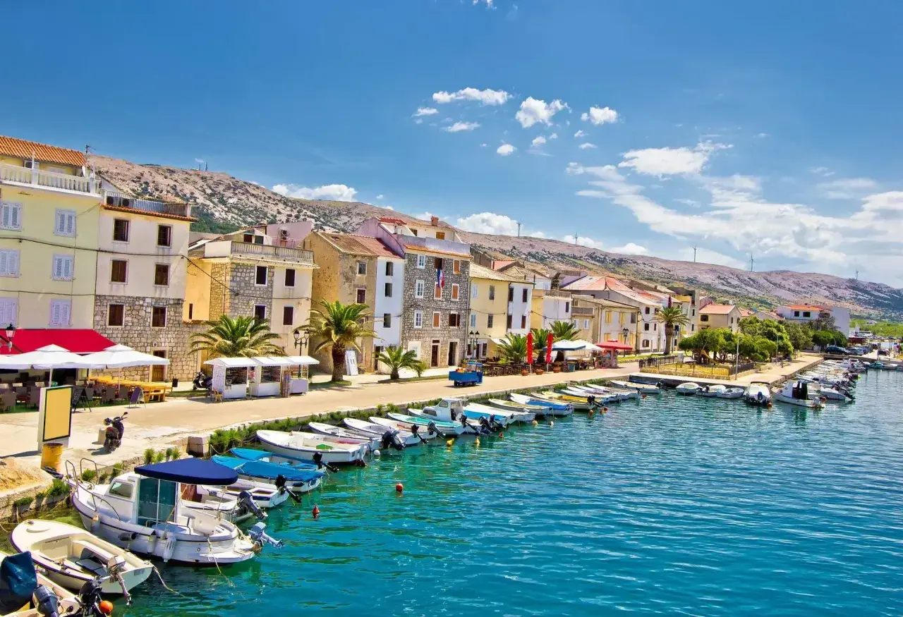 En kuststad i Kroatien med färgglada hus, en hamn full av båtar och en bergig bakgrund. Här finns fakta om Kroatien.