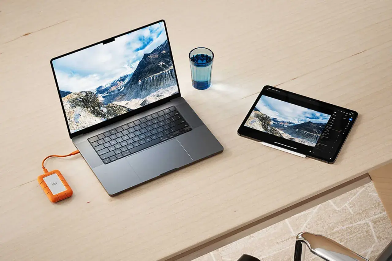 Ein Laptop und ein Tablet mit Berglandschaft, verbunden mit einer externen Festplatte. Ideal für den Datenaustausch zwischen exFAT Windows und Mac.
