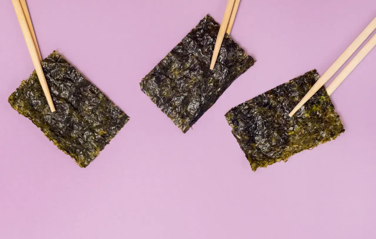 Tre fogli di alga nori, tenuti da bacchette, evidenziano le loro proprietà nutritive.