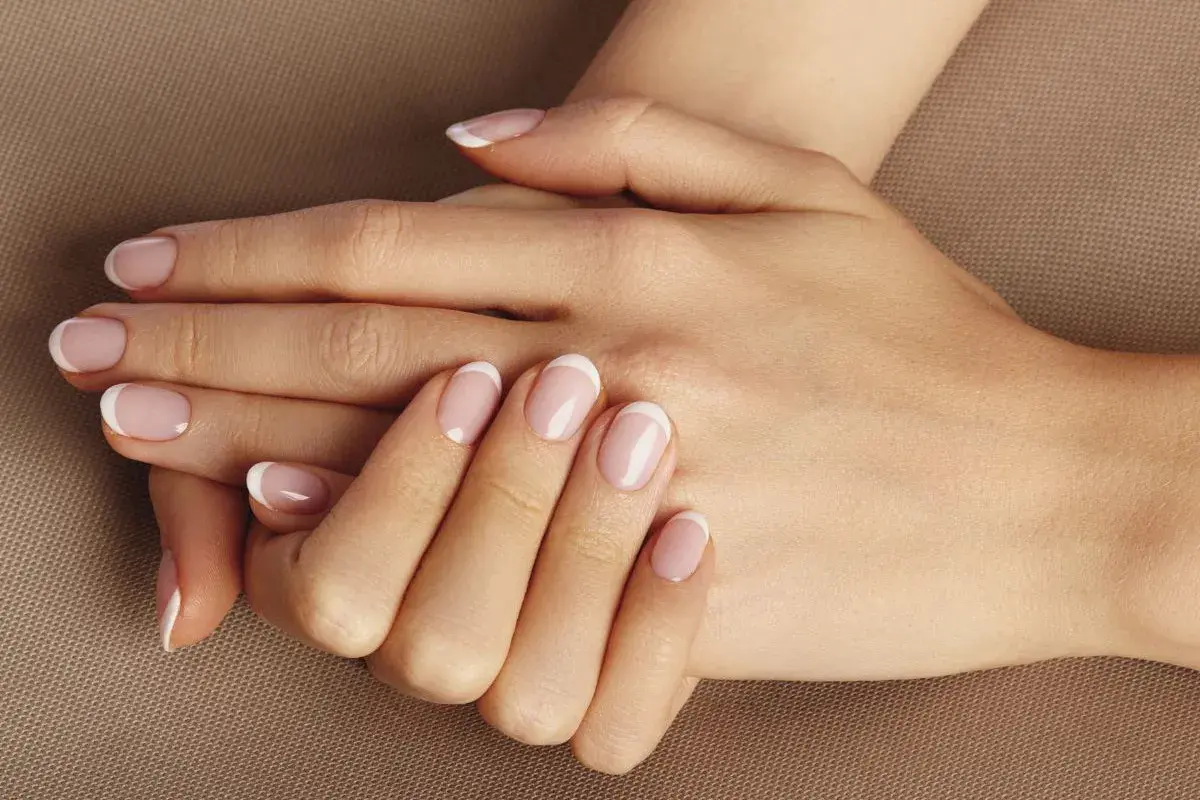 Dłonie z klasycznym francuskim manicure. Delikatny róż i biel na paznokciach, idealne dopełnienie naturalnego piękna. To kwintesencja manicure biologicznego.