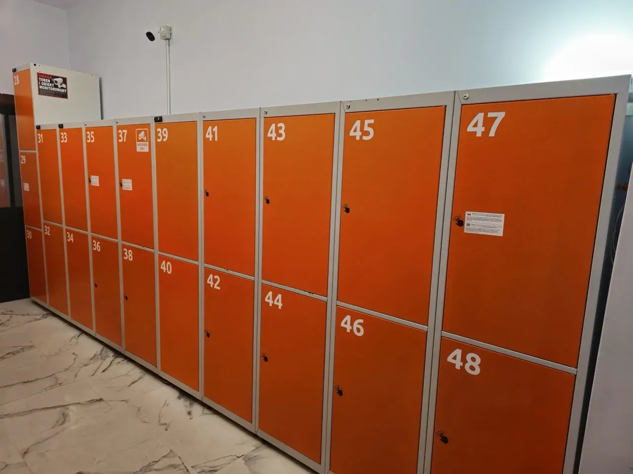 Skrytki bagażowe Kraków Główny: cennik dostępny przy rzędzie pomarańczowych szafek z numerami od 28 do 48.