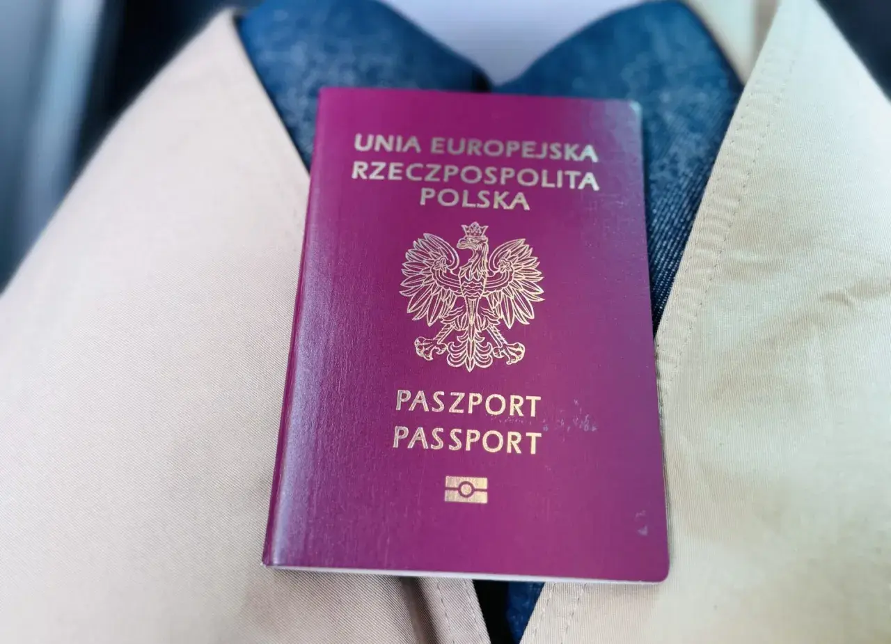 Polski paszport leżący na jasnym płaszczu i dżinsach.