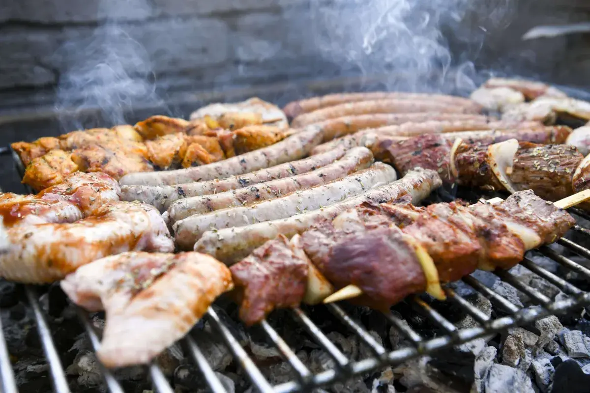 Des saucisses, brochettes de viande et morceaux de poulet à faire un barbecue sur un gril chaud, avec de la fumée qui s'échappe.