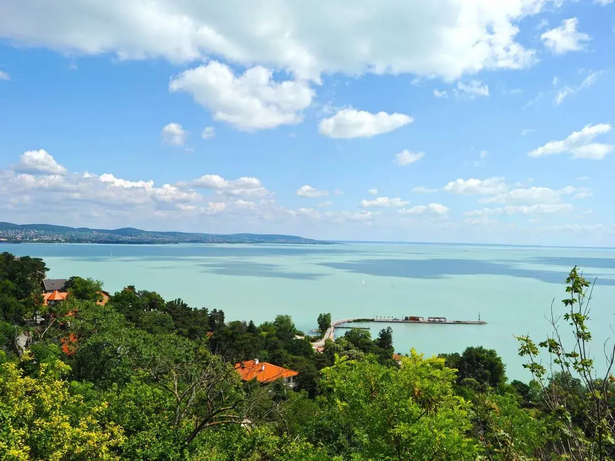 Widok na turkusowe wody Balatonu z zielonymi wzgórzami i domami. To jedno z najpiękniejszych miejsc nad Balatonem, z molo i żaglówkami na horyzoncie.