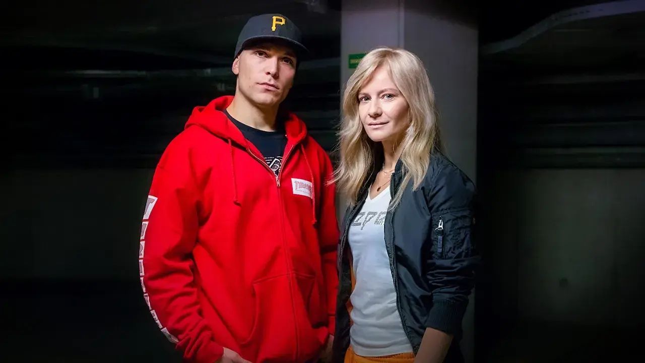 Tomasz Chada z żoną, w ciemnym korytarzu. On w czerwonej bluzie i czapce, ona w czarnej kurtce.