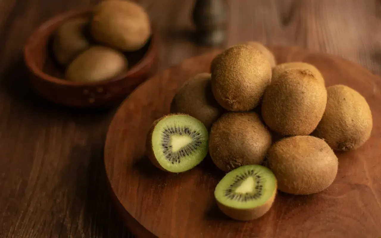 Kiwi, noti per essere tra i cibi che fanno andare in bagno, sono disposti su un tagliere di legno. Uno è tagliato a metà, mostrando la polpa verde e i semi neri.