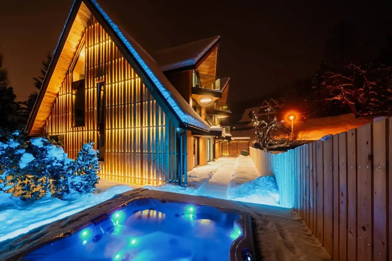 Nowoczesny dom w Zakrzewie oświetlony ciepłym światłem, z podświetlanym jacuzzi w śnieżnej scenerii.